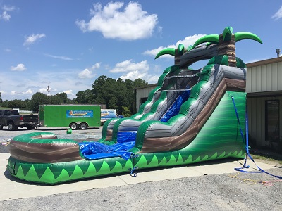 Angled image of the water slide exterior. Two palm trees located on top of the water slide with a pool attached at the bottom of the slide.