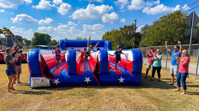 Patriotic red white & blue Bungee Run inflatable setup outdoors with kids playing from Austin Bounce House Rentals™