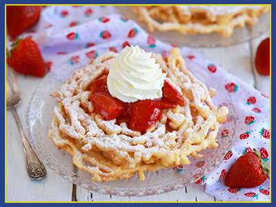 Plated funnel cake with powder sugar, strawberries, and whipped cream.