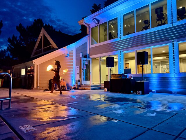DJ in the background of a luau while a man dances with fire.