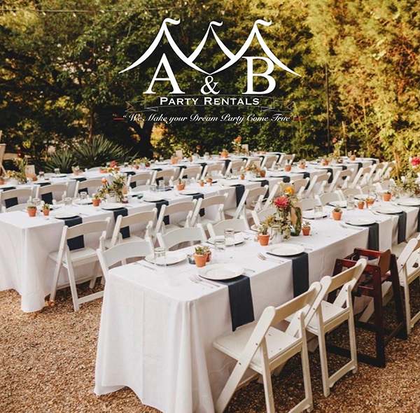 A rustic outdoor wedding reception featuring long rectangular tables with white linens, plates, silverware, white folding chairs, and floral centerpieces. The image captures a charming rustic outdoor wedding reception setting with long rectangular tables elegantly dressed in white linens, complete with place settings, white folding chairs, and beautiful floral centerpieces. This picturesque scene is provided by A&B Party Rentals in Salisbury, MD.