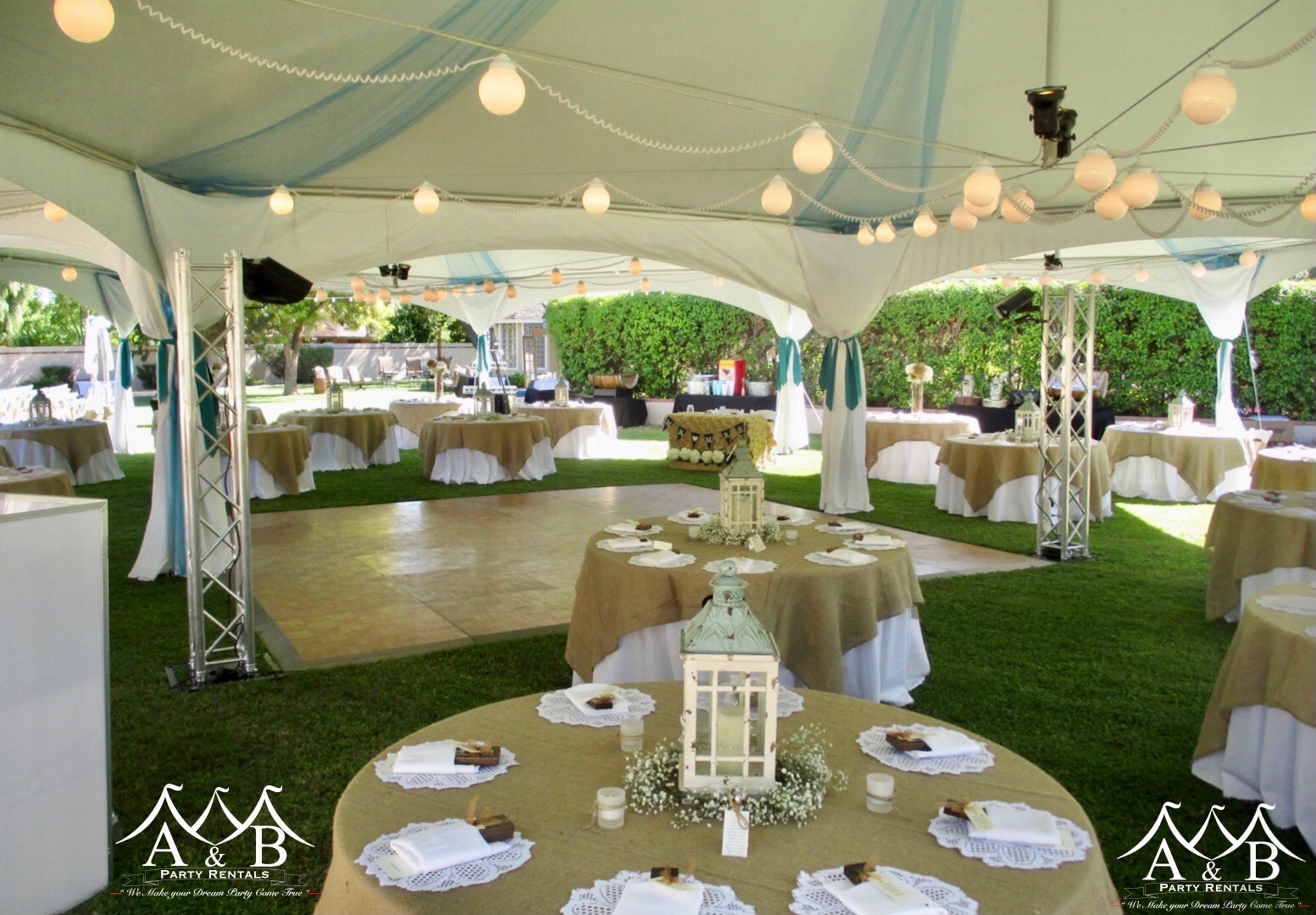 A daytime outdoor wedding reception under a tent featuring tent lights, a dance floor, tables with elegant linens, and place settings. The image captures an idyllic outdoor wedding reception setting under a tent, adorned with lights, a dance floor, well-appointed tables showcasing elegant linens, and meticulously arranged place settings. This picturesque scene is provided by A&B Party Rentals in Salisbury, MD.
