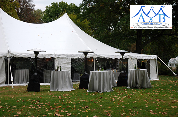 A large outdoor formal event or wedding reception featuring clear side walls, tables draped in gray linens, and large mobile heaters. The image showcases an elegant outdoor setting with clear side walls enclosing the space, tables dressed in sophisticated gray linens, and strategically placed large mobile heaters providing warmth for guests. Create a stylish atmosphere for your events with these rental options from A&B Party Rentals in Salisbury, MD.