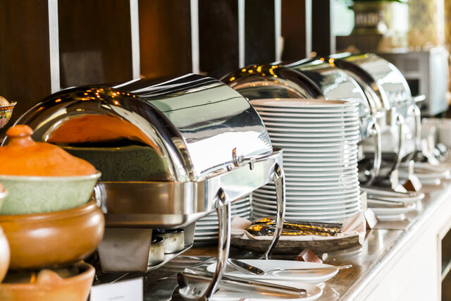 Catering table filled with chafing dishes, plates and cutlery