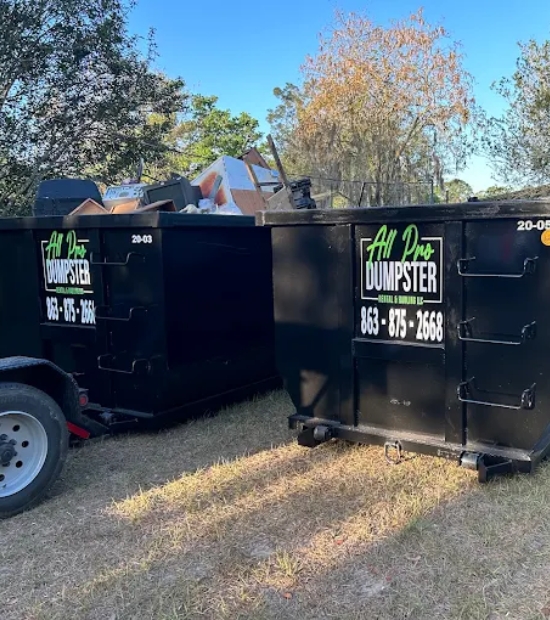 Two black roll-off dumpsters from All Pro Dumpster Rental & Hauling, LLC filled with debris at a residential cleanup site Two black roll-off dumpsters from All Pro Dumpster Rental & Hauling, LLC filled with debris at a residential cleanup site