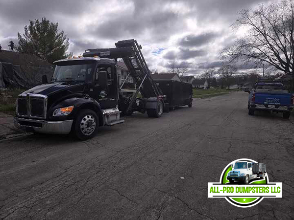 Professional pickup of a loaded roll-off container by All Pro Dumpsters' hydraulic lift truck, showing their reliable removal service