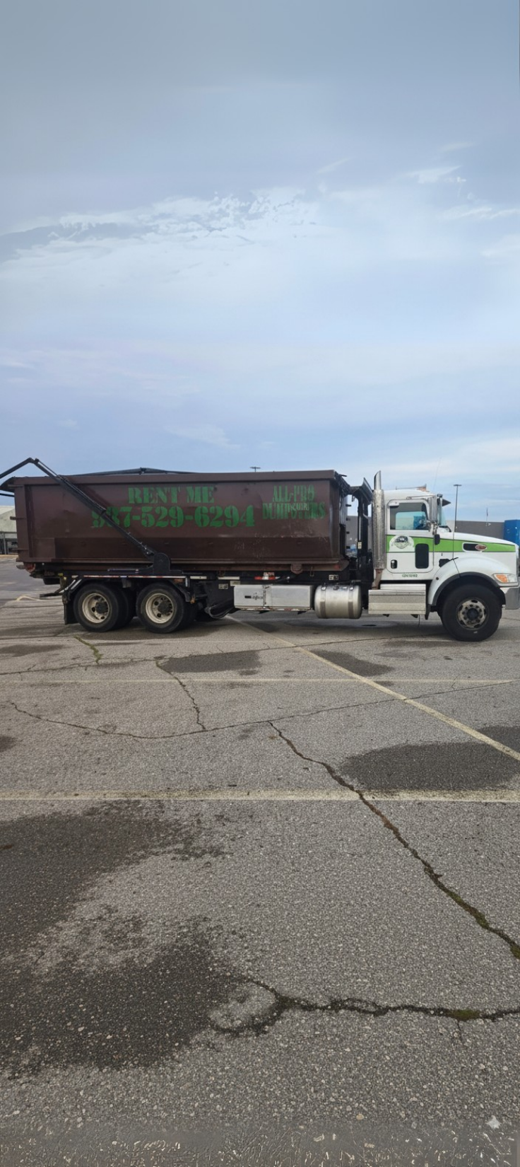 A brown roll-off dumpster for rent from All-Pro Dumpsters loaded on a white truck.