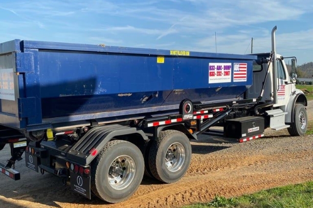 A roll-off truck from American Dumpster Company hauling a blue dumpster