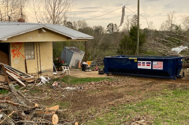 A roll-off dumpster from American Dumpster Company beside storm debris