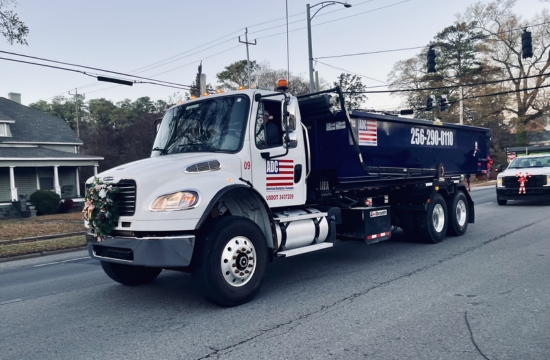 An American Dumpster Company roll-off truck driving on a city street