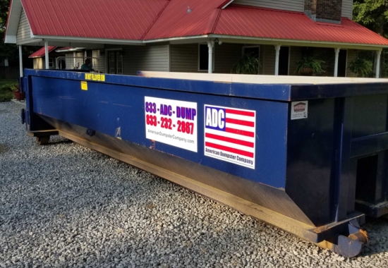 A blue roll-off dumpster from American Dumpster Company on a gravel driveway