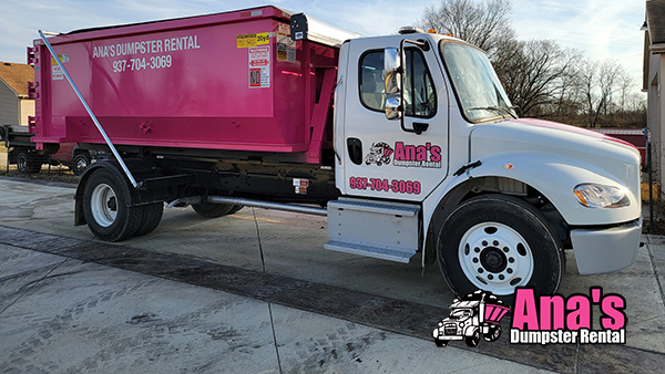 Pink roll-off dumpster truck parked on driveway — Ana's Dumpster Rental