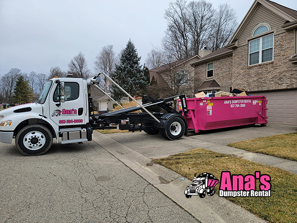 Ana's Dumpster Rental truck dropping off a pink dumpster at a residential home