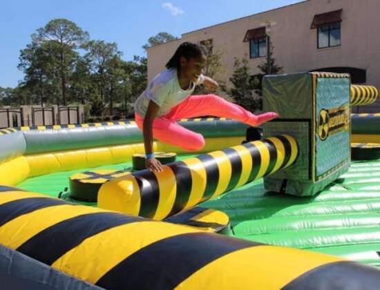 Girl jumping over a rotating inflatable obstacle on a yellow and black meltdown ride at an outdoor event