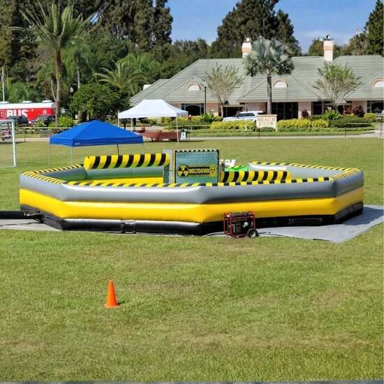 Girl jumping over a rotating inflatable obstacle on a yellow and black meltdown ride at an outdoor event