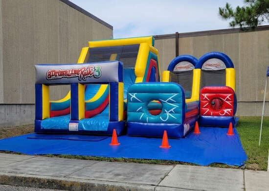 Red and blue inflatable bounce house castle with turrets set up in a parking lot, surrounded by orange safety cones
