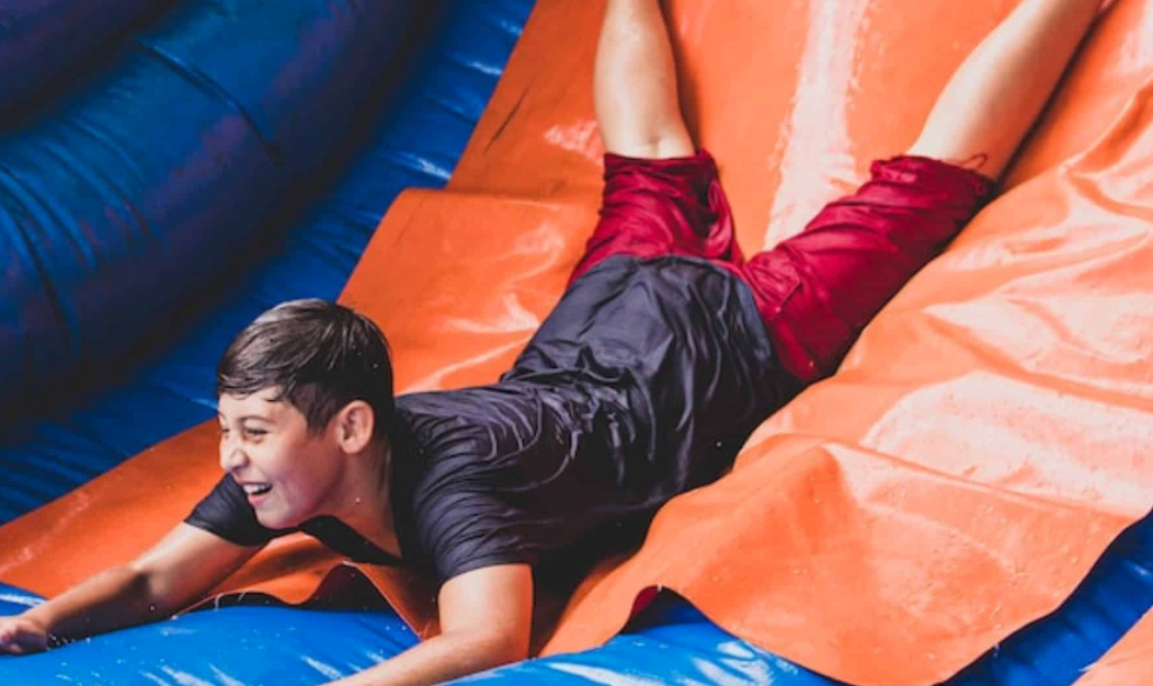 A smiling child slides down a colorful inflatable water slide, showing the kind of refreshing summer fun A Party Solution brings to birthday parties, school events, church gatherings, and family celebrations in Cedar Hill, TX.