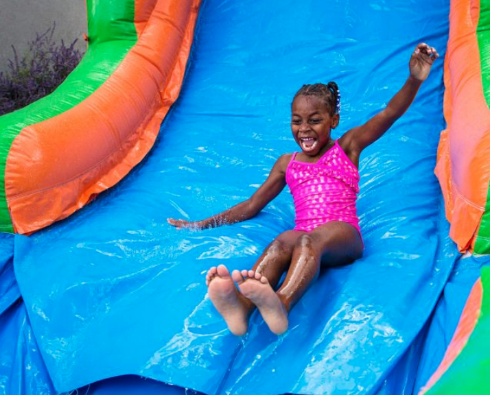 A happy child slides down a bright blue inflatable water slide with orange and green accents. This image highlights the fun, family-friendly water slide rentals A Party Solution provides for Midlothian, TX backyard parties, church events, school fun days, and warm-weather community gatherings.