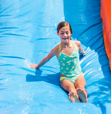 Child smiling while sliding down a colorful inflatable water slide rental in Midlothian, TX from A Party Solution.