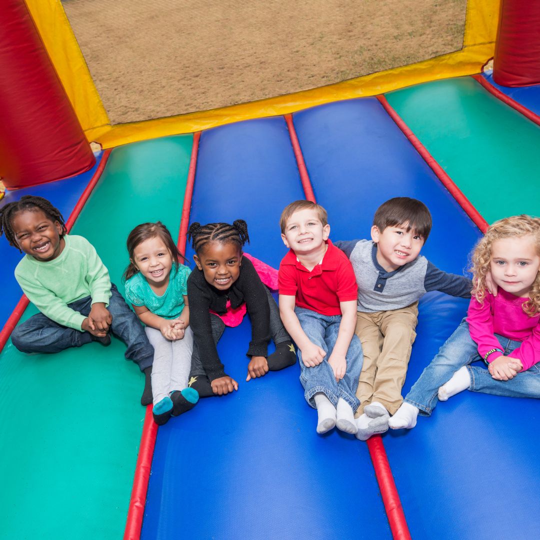 Kids sitting and smiling inside a colorful inflatable bounce house from our bounce house rentals in Grand Prairie, TX.