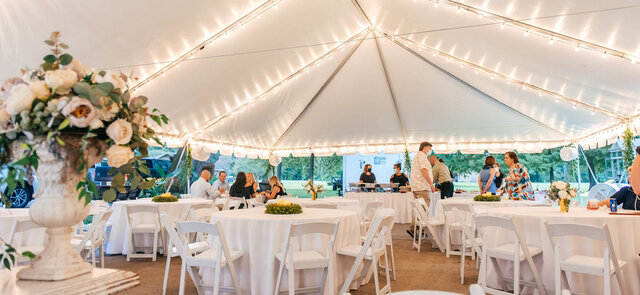 Elegant wedding reception under a white tent with string lights, round tables, and white folding chairs