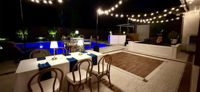 Backyard evening party setup with string lights, dining tables, and a poolside dance floor