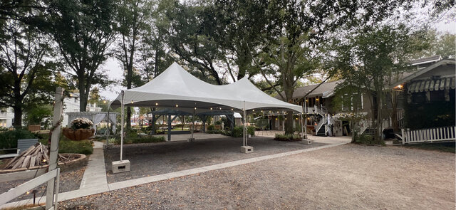 White high peak tent set up in a rustic outdoor venue with trees and surrounding buildings