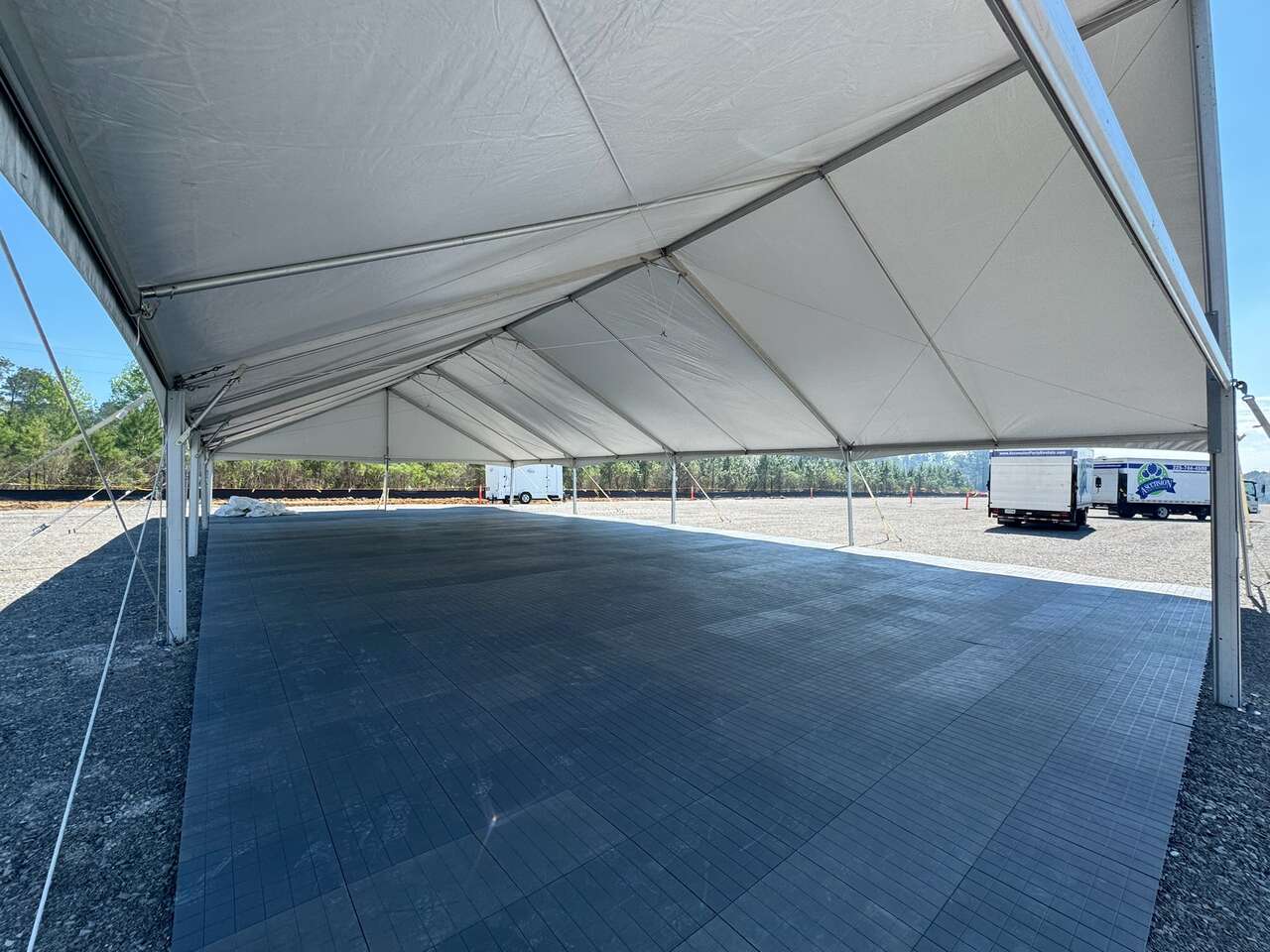 Large industrial frame tent with modular flooring installed over gravel at a construction site