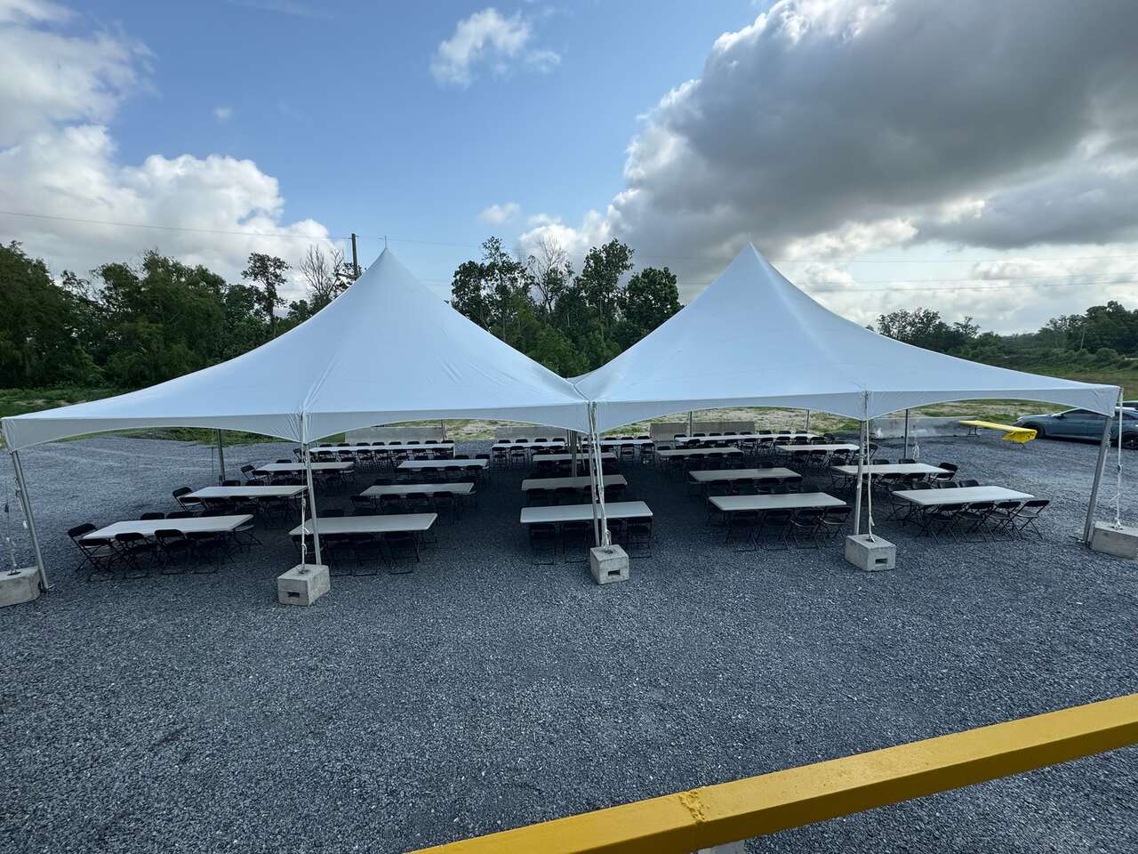 Large frame tent with tables and chairs set up for a plant crew meal on gravel
