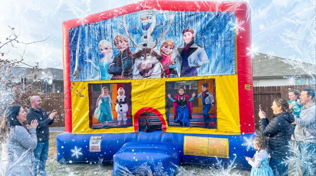 Frozen themed bounce house setup outdoors with kids playing, parents watching.
