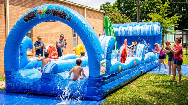 Surf the Wave Slip'n Slide inflatable setup outdoors with kids playing and parents watching.