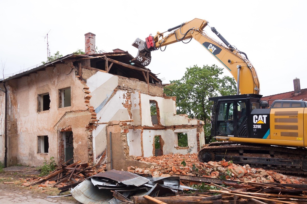 Excavator demolishing an old brick building with debris scattered around.