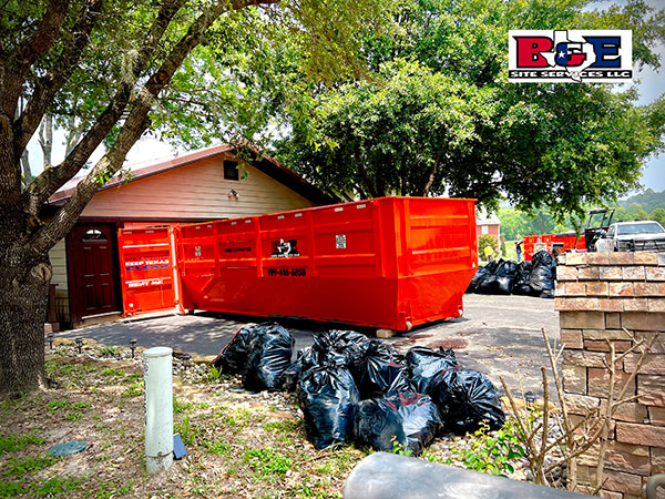 Red dumpsters near a house with trash bags.