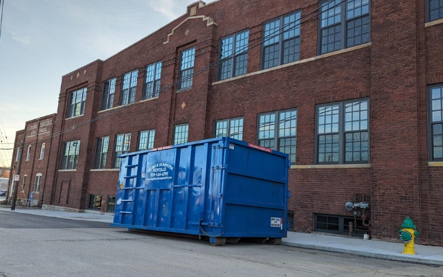 Blue Big Blue Dumpster positioned by a commercial building for routine business waste service