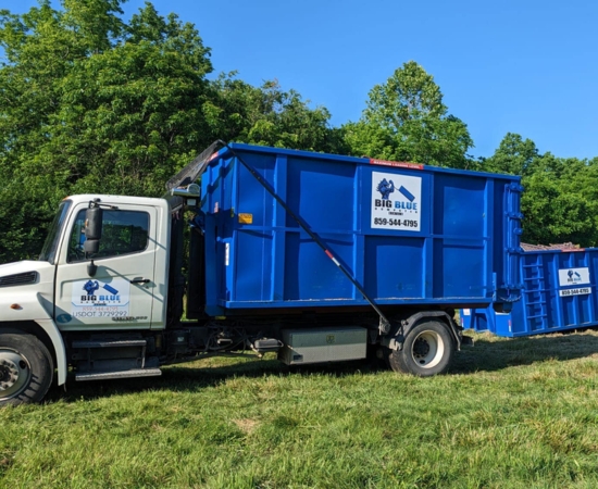 Big Blue Dumpster truck positioned on grass carrying a blue roll-off container Big Blue Dumpster truck positioned on grass carrying a blue roll-off container