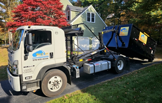 Big Foot Dumpsters truck delivering a roll-off dumpster in a residential driveway
