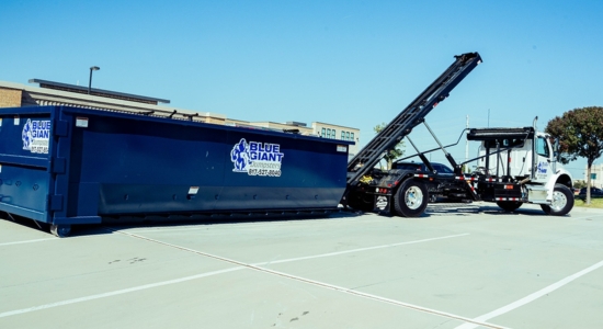 Blue Giant Dumpsters roll-off container being loaded onto a truck in a parking lot.