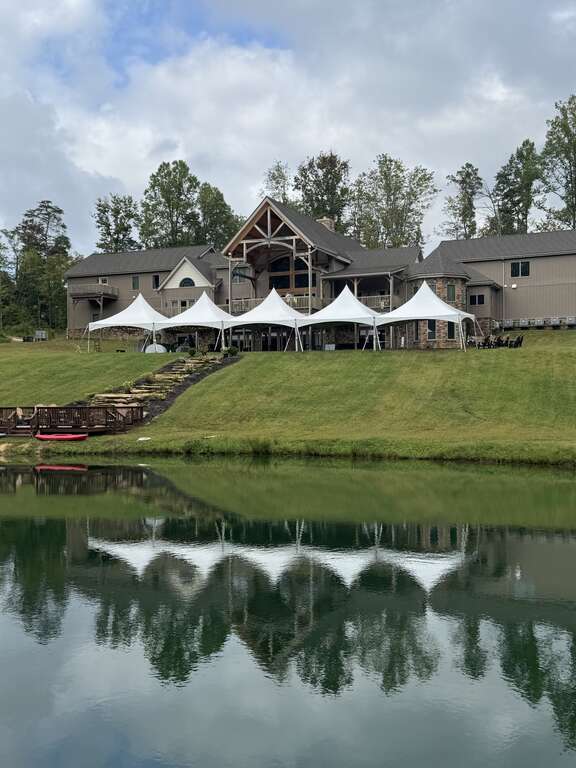 Five high peak tents on a hill above a pond