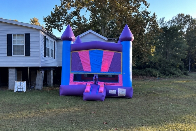 Purple and blue bounce house rental from Boomin Bounce set up on a grassy backyard lawn