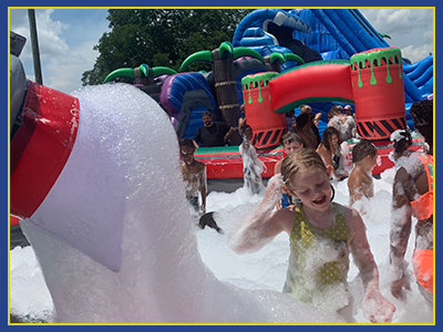 View of a child playing in front of a foam machine with children in the background.