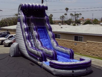 Angle view of a 22 foot inflatable waterslide that is granite in color with purple trim.