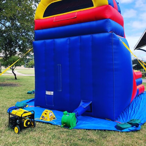 Portable generator being used to supply electricity to 16-foot inflatable slide on grass in park.