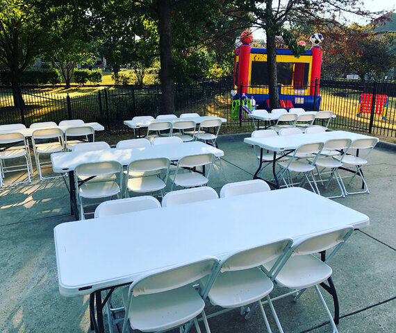 6-foot rectangular white tables with white folding chairs in front of sports arena bounce house in backyard party.
