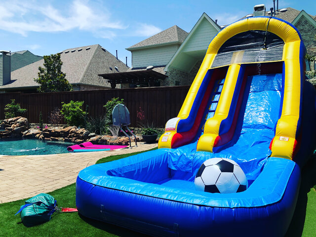 14-foot inflatable water slide with pool on artificial turf anchored with sandbags next to inground pool