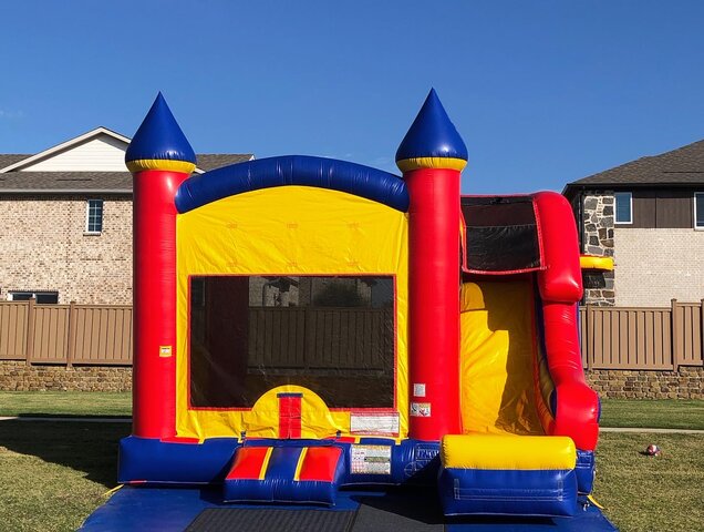 Inflatable bounce house with slide and basketball hoop on grass at a school event.