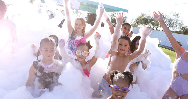 Group of children at a foam party playing inside the foam pile in a backyard on artificial turf near Frisco Texas.