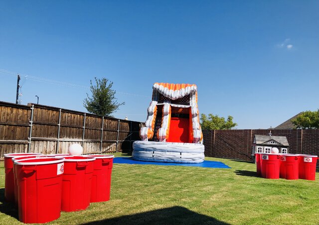 Giant beer pong on grass with 15-foot water slide with pool in backyard for party.