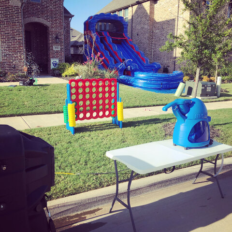 Sno cone machine, bubble machine, outdoor air conditioner, connect 4 game, and 15-foot red white and blue water slide with pool on grass for HOA event.