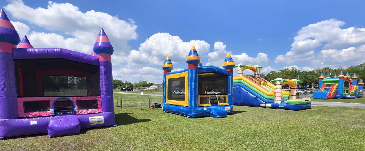 Purplish and Melting Arctic bounce houses, the 16 FT Adventure Island double slide and the 50' Multi Color Obstacle Course set up on a grass field for a church Candy Drop in Kissimmee, FL