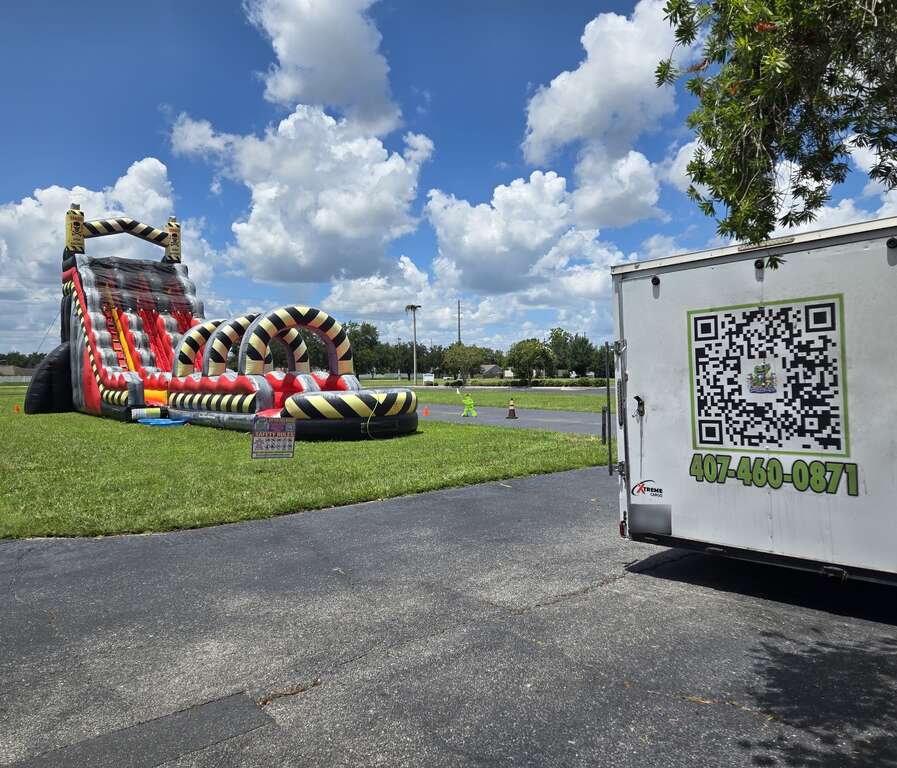 32-foot Nuclear Toxic double-lane water slide with pool on a church lawn in Saint Cloud, FL, beside the Bounce N Around Rentals trailer